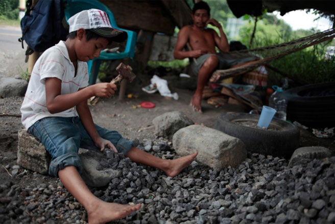 Cậu bé Josue Alexander Chavez (trái), 9 tuổi, đang dùng búa để đập vỡ những tảng đá tại một cơ sở sản xuất đá xây dựng ở Guatemala. Josue làm việc cùng với cha mẹ của em, hàng ngày từ 7h sáng đến 5h chiều, kiếm được khoảng 2,5 USD mỗi ngày - Tin: WSJ/Ảnh: Reuters.