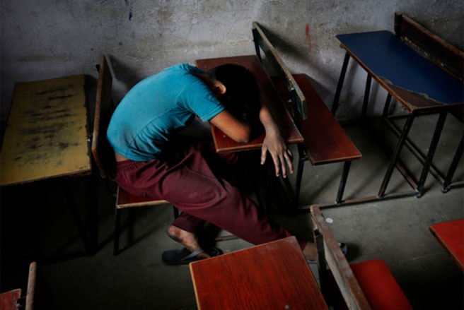 Một công nhân “tí hon” ngủ gục trên bàn học trong một ngôi nhà an toàn sau khi được giải cứu bởi Phong trào Hãy cứu lấy tuổi thơ sau một cuộc tấn công vào một nhà máy dệt may ở New Delhi, Ấn Độ vào tháng 6/2013 - Tin: WSJ/Ảnh: AP.