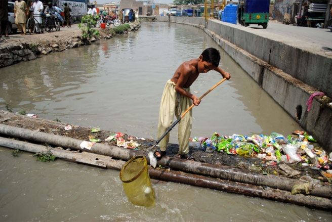Một em bé đang làm công việc làm sạch một con kênh đầy rác rưởi ở Peshawar, Pakistan vào tháng 6/2013 - Tin: WSJ/Ảnh: Zuma Press.