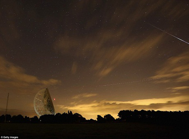 Một bức ảnh chụp chậm cho thấy ngôi sao băng bay ngang qua bầu trời cùng lúc với vệt sáng để lại của một chiếc máy bay.