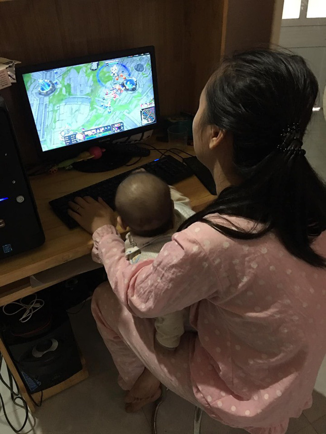 Người mẹ bế con nhỏ rồi chơi game.