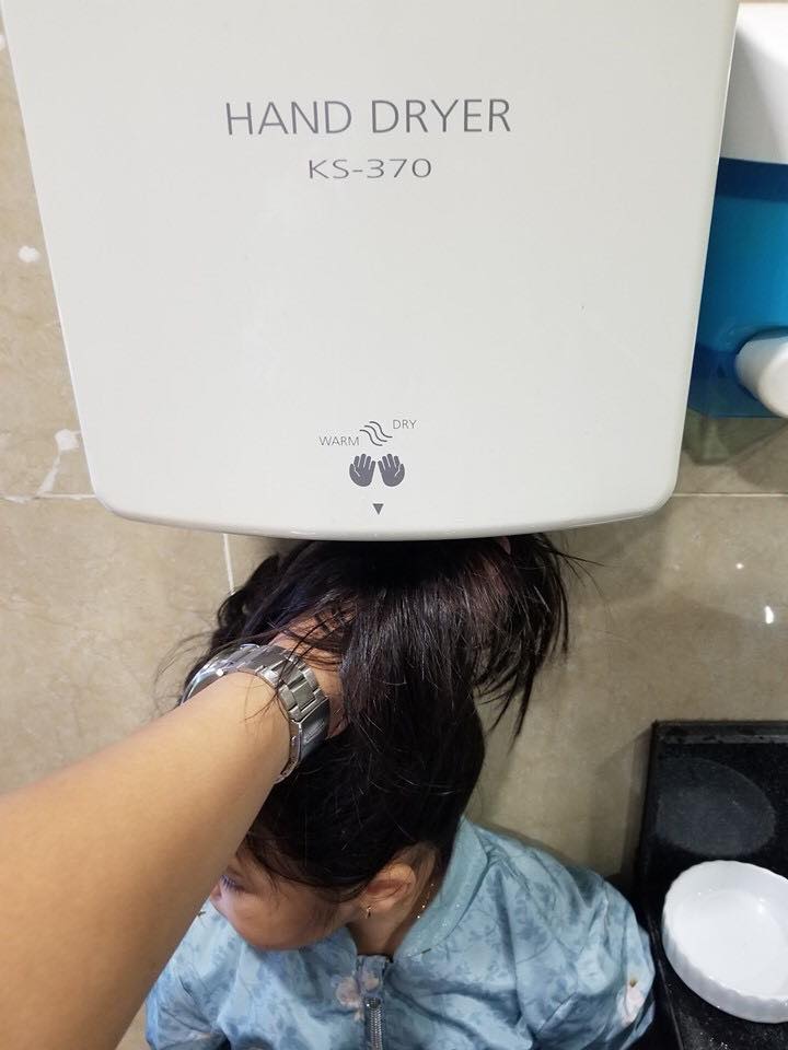 Ông bố dùng máy sấy tay để sấy tóc cho cô con gái.