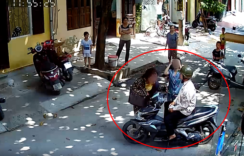 Người chồng ngồi trên xe máy mặc vợ đang bị đánh.
