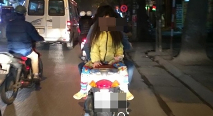 Bố mẹ thản nhiên để con gái ngồi quay ngược lại trên xe máy.