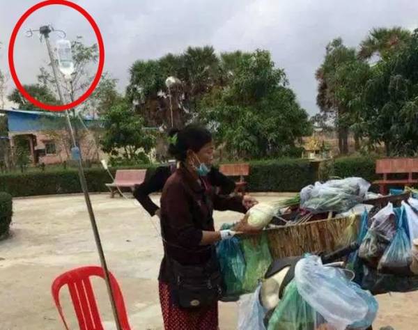 Người phụ nữ vừa truyền dịch vừa bán rau ở đường.