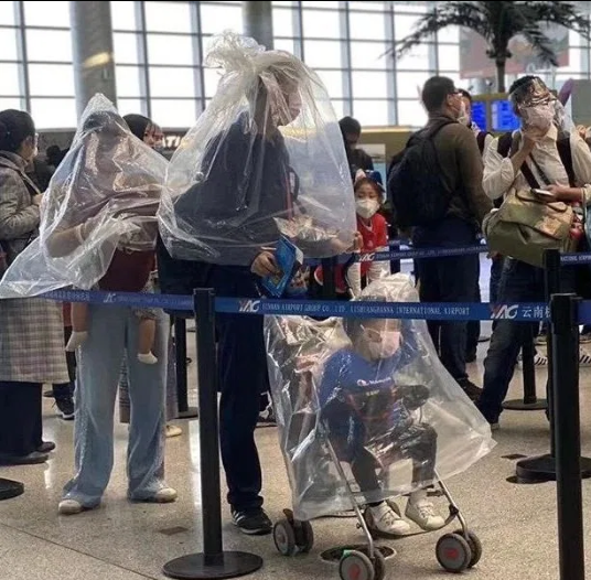 Một gia đình trùm túi nilon kín mít khi đứng chờ ở sân bay.