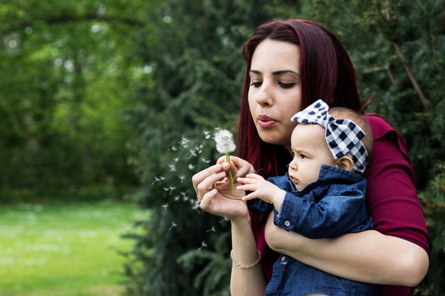 woman-holding-baby-while-blowing-dandelion-2224959