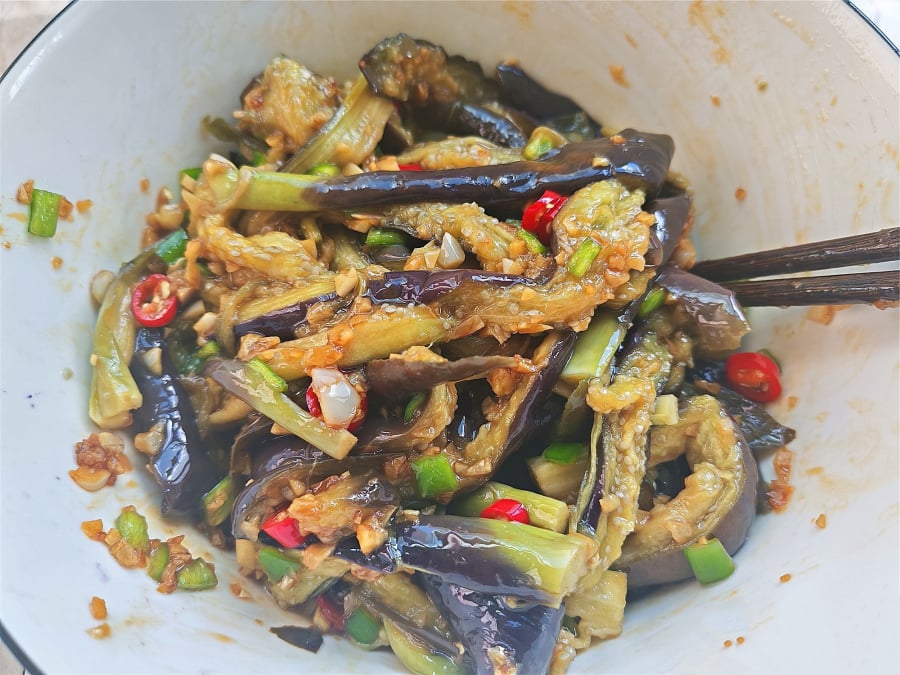 Cà tím sau khi hấp chín, được xé nhỏ và trộn cùng nước sốt cay nồng từ tỏi và ớt – từng sợi cà mềm thơm, thấm đẫm gia vị.