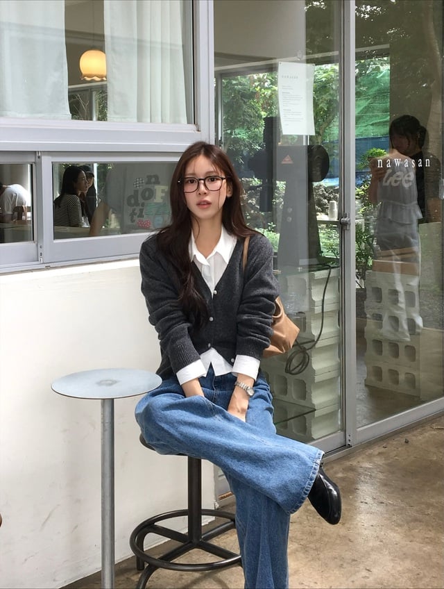 Sự kết hợp giữa áo sơ mi trắng, cardigan xám và quần jeans xanh là công thức “an toàn” mà vẫn ghi điểm tuyệt đối.