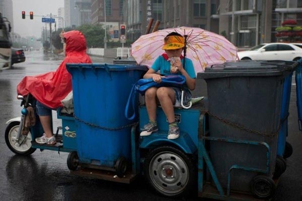 Vào một ngày mưa tại Bắc Kinh, một bé trai đang vui vẻ ngồi thưởng thức bữa sáng của mình bên cạnh những thùng rác...