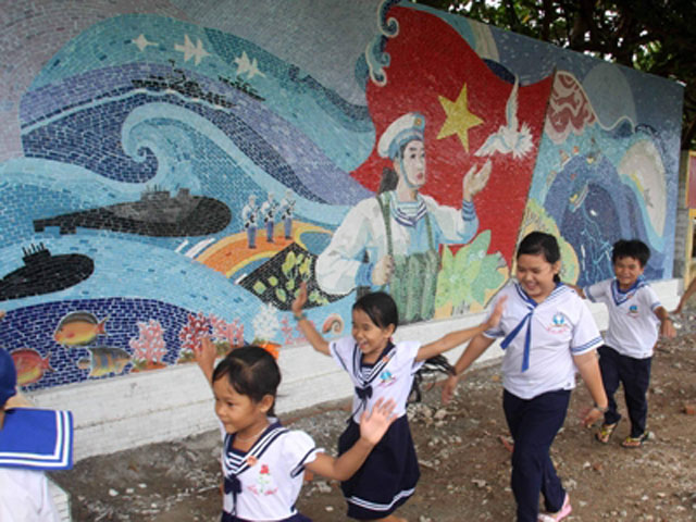 Hai bức tranh phía sau là cảnh làng quê Việt Nam thân thuộc; một bức là hoa sen, hoa đào, hoa mai, gợi những hình ảnh thân quen hiện diện trong cuộc sống hàng ngày của các chiến sĩ. Trẻ nhỏ trên đảo chơi cạnh các bức tường gốm được xây dựng đồng thời với lá cờ. Ảnh: Tạ Ngọc Hưng (VOV) và Trần Việt (TTXVN)
