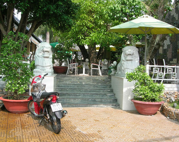  Tại quán Cánh Buồm của ông Tân, người ta có thể chiêm ngưỡng cách bố trí, trưng bày nội thất trị giá vài trăm, thậm chí cả tỷ đồng. Theo các tay chơi ở TP Sóc Trăng, ông Tân là   người rất “mê” thuật phong thủy. Sao một thời gian quán Cánh Buồm làm ăn ế ẩm, ông Tân cho xây dựng cả một bức tường rộng lớn ở phía bên phải của quán, rồi thuê họa sĩ về vẽ cả   một bức “Vạn lý trường thành” để thị uy cho vị thế không gì thay đổi được của mình. Cặp sư tử đá này được Tân “ròm” đặt trước quán cà phê Cánh Buồm Xanh ở Tp Sóc Trăng.
