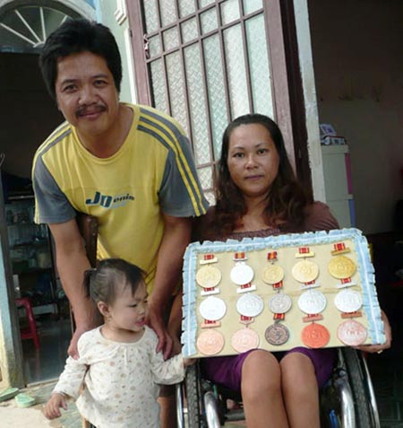 Vợ chồng anh Long cùng đứa con út nhặt được cùng các thành tích thể thao khuyết tật của hai vợ chồng.