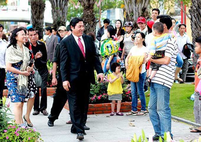Ông Nguyễn Bá Thanh nở nụ cười với một em nhỏ được bố bế trên tay. Trên đường hoa, ông và người dân cùng bắt tay, trò chuyện.