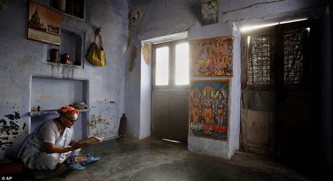 Một góa phụ cao cuổi đang đọc sách thánh trong một căn phòng được trang trí bằng những hình ảnh của đạo Hindu.
