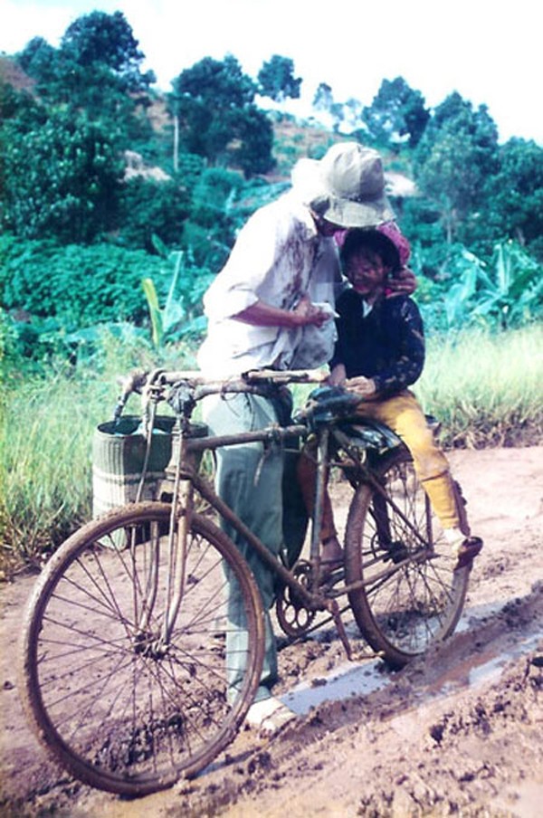 Hai cha con bên chiếc xe đạp cũ, vượt qua đoạn đường bùn lầy. Cha ân cần lấy áo lau bùn trên mặt con gái.