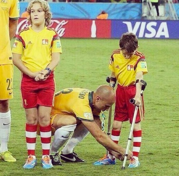 Tiền vệ Mark Bresciano của đội tuyển Úc gây ấn tượng mạnh với giới truyền thông sau hành động ngậm cờ trong miệng để có đủ tay giúp cậu bé mascot chống nạng buộc dây giày.