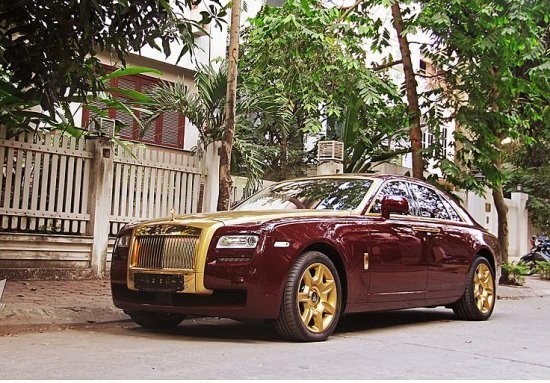 Chiếc Rolls-Royce Ghost của một đại gia ở Hà Nội có nước sơn màu đỏ mận và lớp áo mạ vàng chạy từ mép trần kính chắn gió, qua ca-pô xuống hết mặt tản nhiệt với các thanh chắn hình lò sưởi đặc trưng.