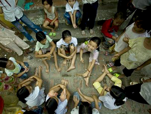 2-5 bé gái ngồi vòng tròn với 10 que tre nhỏ và một quả cà chơi trò đánh chuyền.