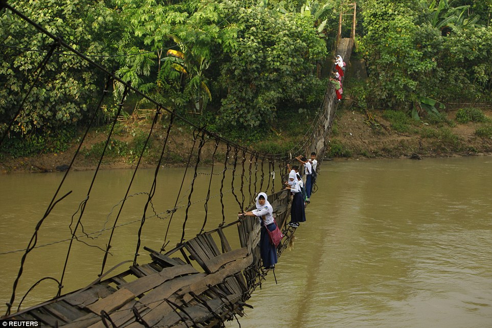 Các học sinh phải bám vào dây thép của một cây cầu bị hỏng để qua sông Ciherang tới trường ở Lebak, Indonesia.
