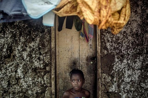 Một bé gái ngồi một mình trước căn nhà lạnh lẽo sau khi bố mẹ qua đời vì Ebola ở ngôi làng Njala Ngiema (Sierra Leone).