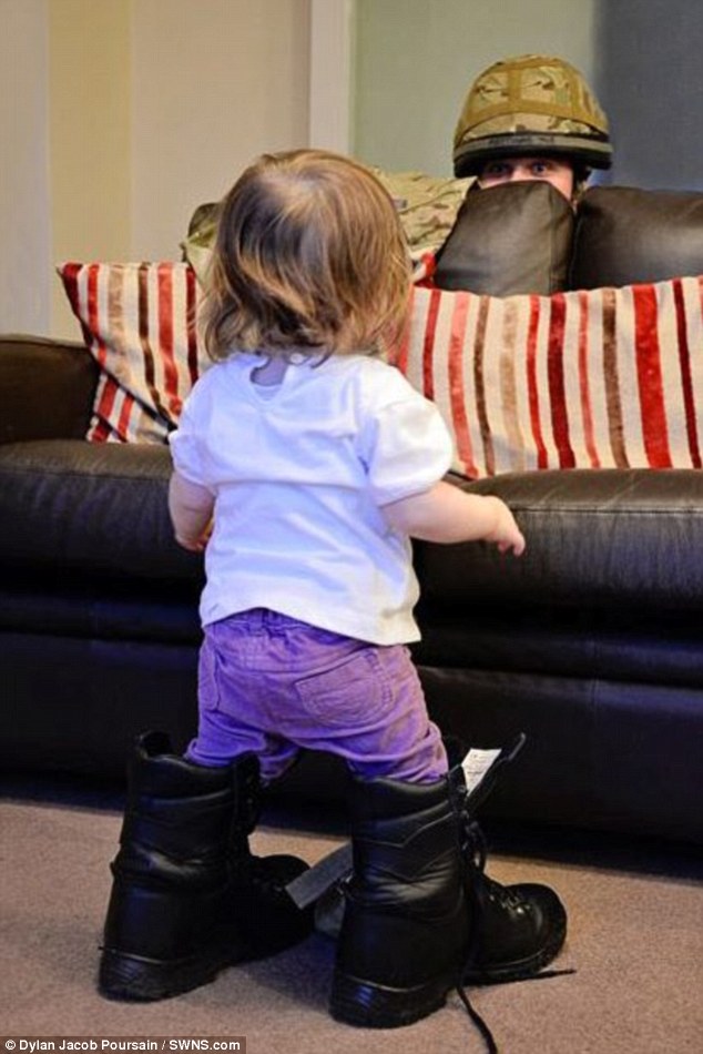 Bé gái Isabella thử đôi giày của bố, trong khi bố trốn sau ghế sofa.