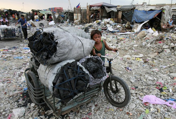 Một bé trai đang đẩy một chiếc xe chứa đầy bao tải đựng than tại khu vực tập trung rác thải ở Tondo, Philippines.
