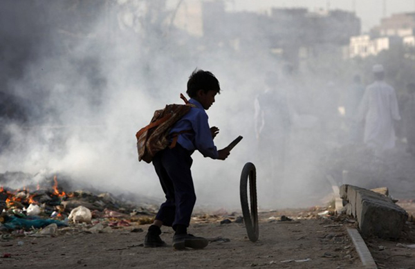 Một bé trai tại khu ổ chuột ở Karachi, Pakistan sử dụng chiếc que nhỏ và lốp xe hỏng để tự tạo trò chơi cho riêng mình.