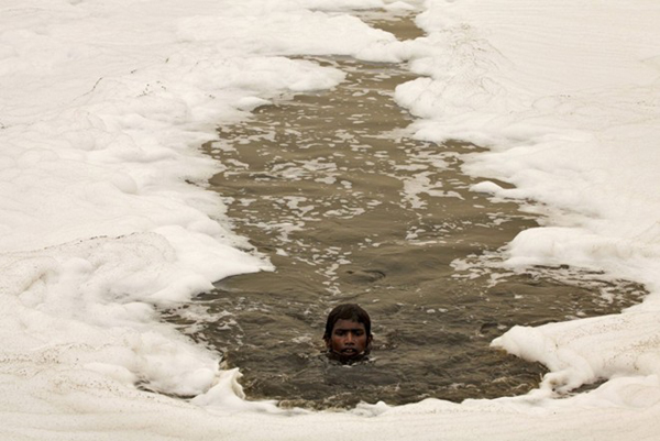 Một cậu bé đang bơi qua dòng sông Yamuna đầy bùn và bọt, chất thải từ các nhà máy công nghiệp, ở New Delhi, Ấn Độ.
