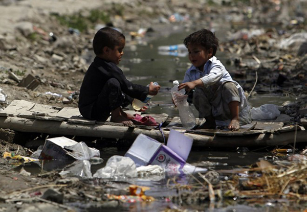 Hai bé trai đang cố gắng múc đầy bình nước tại một rãnh nước bẩn ở Kabul, Afghanistan.