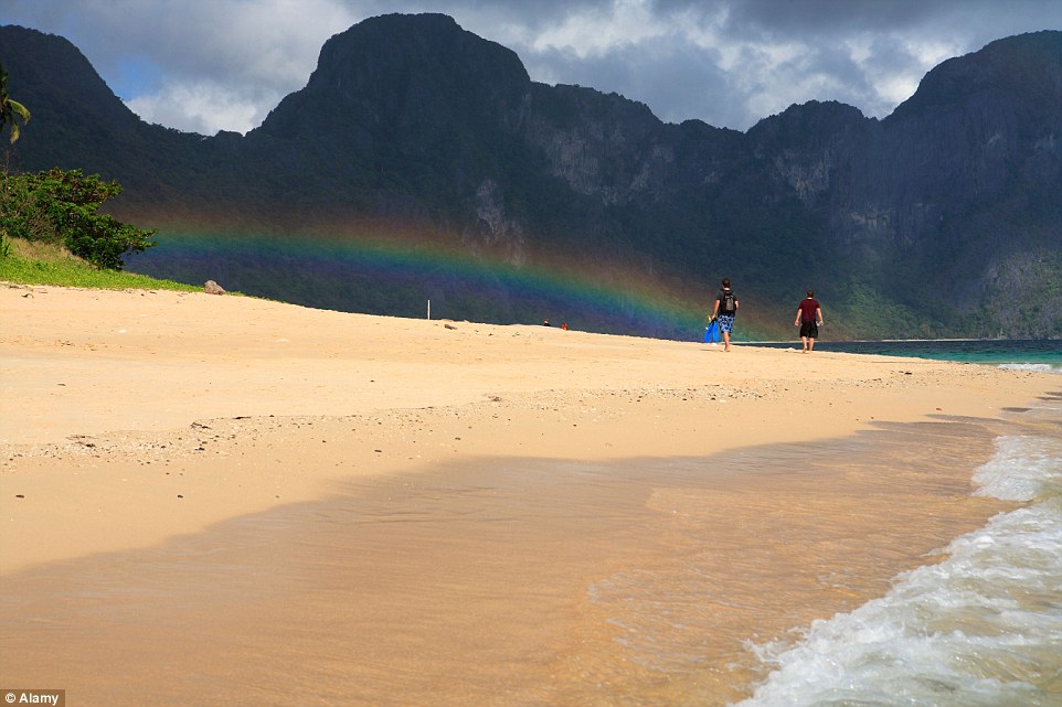 Du khách đi bộ trên bãi biển khi cầu vồng hình thành ở phía xa.