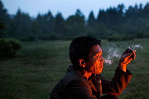 Một người đàn ông hút thuốc trong khi nhóm lửa để nướng khoai và gà tại thị trấn Samjiyon, tỉnh Ryanggang.