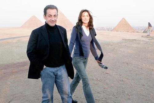 Tổng thống Pháp Sakory phong độ và sành điệu bên cạnh vợ trẻ khi mặc jeans mài gối vơi áo pull đen và vest đen.