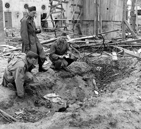 Phóng viên chiến tranh của tạp chí LIFE Percy Knauth (trái) nhìn đống rác thải ở một rãnh nước trong vườn của Thủ tướng Đức. Vị trí này được cho là nơi chôn cất xác của Hitler và Eva sau khi hai người tự sát.