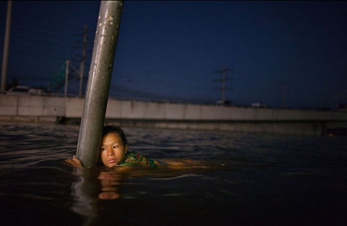 Một người phụ nữ bám lấy cột báo hiệu đường phố để khỏi bị cuốn trôi trong trận lụt ở ngoại ô Bangkok, Thái Lan năm 2011.