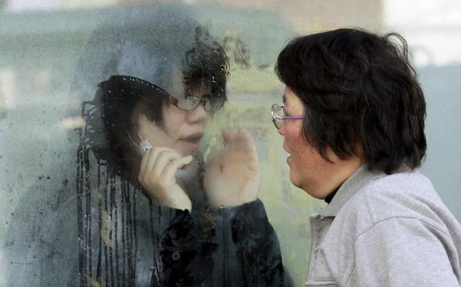 Một phụ nữ cố nói chuyện với con gái qua lớp kính. Cô gái bị cách ly vì có mặt trong khu vực nhiễm phóng xạ của nhà máy Fukushima.
