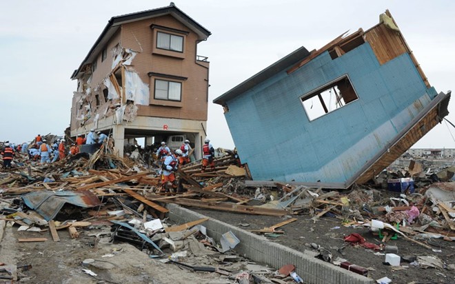 Lực lượng cứu hộ tìm người sống sót trong những căn nhà bị tàn phá nghiêm trọng ở Natori, tỉnh Miyagi. Lượng nước khổng lồ tràn vào từ biển khiến những ngôi nhà gỗ bị lật ngửa.