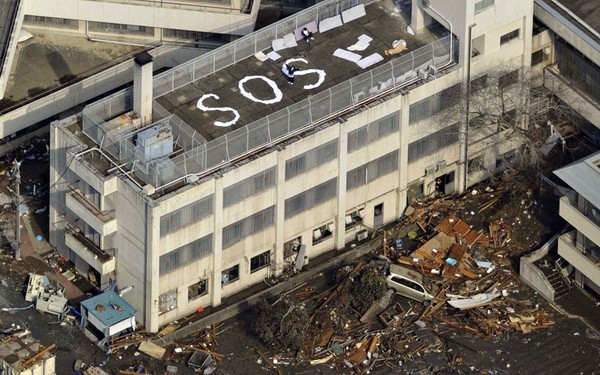 Người dân Kesennuma, quận Miyagi đứng trên nóc nhà chờ đợi cứu trợ cùng dòng chữ 'SOS'.