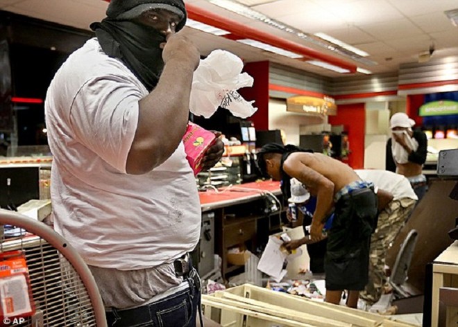Một tên cướp giấu súng trong cạp quần, lấy hàng tại cửa hàng QuikTrip sau khi bạo loạn nổ ra tại lễ đốt nến tưởng niệm Michael Brown ở thành phố Ferguson, bang Missouri, Mỹ.