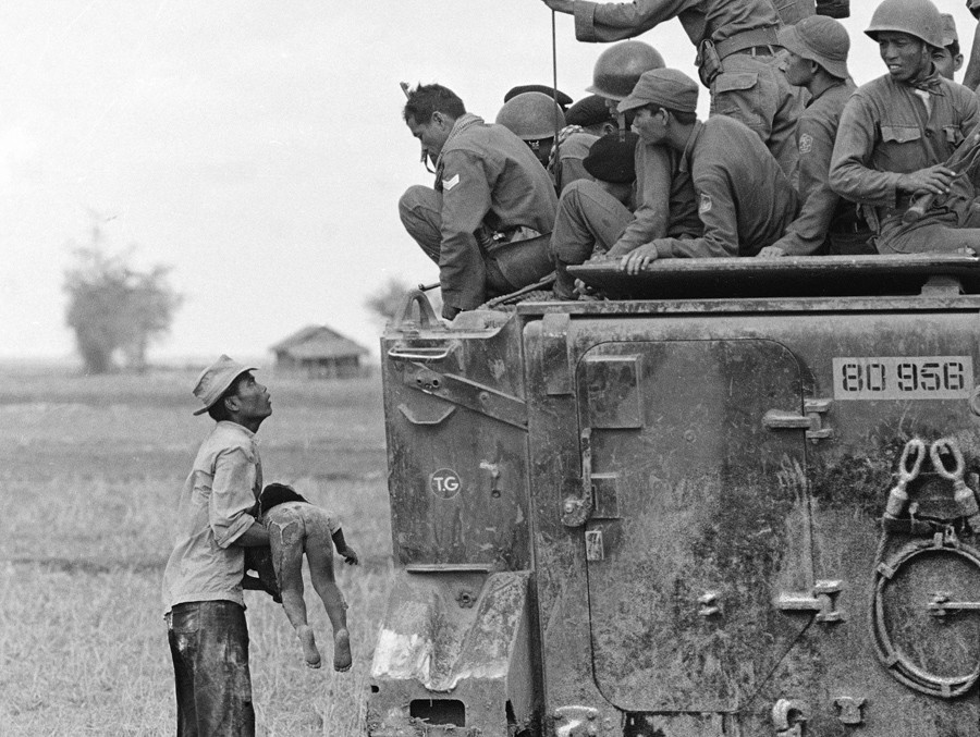 Người cha mang thi thể đứa con nhỏ tới cạnh xe bọc thép chở lính VNCH. Đứa trẻ thiệt mạng sau trận càn của lực lượng này qua ngôi làng của họ ở gần biên giới Campuchia tháng 3/1964.