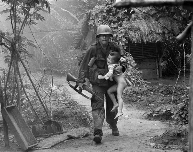 Lính bộ binh Mỹ bế một đứa trẻ ra khỏi làng Cam Xe, gần đồn điền cao su Michelin Dầu Tiếng, phía tây bắc Sài Gòn, sau vụ tấn công ngày 22/8/1966. Ảnh: AP