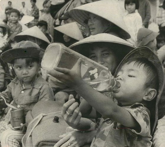 Trong cơn khát, một bé trai uống nước từ chai rượu cũ. Cậu bé cùng gia đình tập trung tại một sân bóng ở Kom Tum để chờ di tản khỏi vùng chiến sự, ngày 7/6/1972. Ảnh: AP