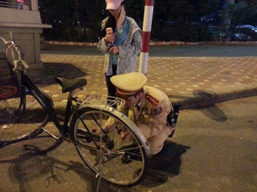 Một cảnh sát giao thông cặm cụi sửa xe đạp giúp cô gái trẻ.