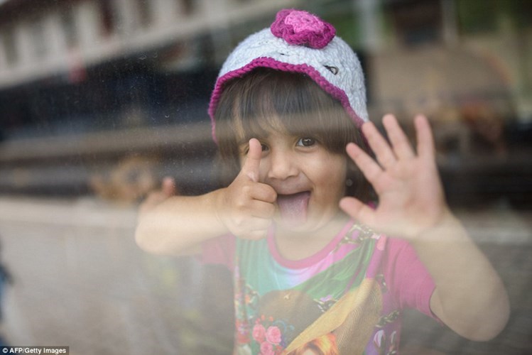 Một bé gái tị nạn sung sướng giơ ngón tay cái sau khi lên tàu thành công. (ảnh: AFP)