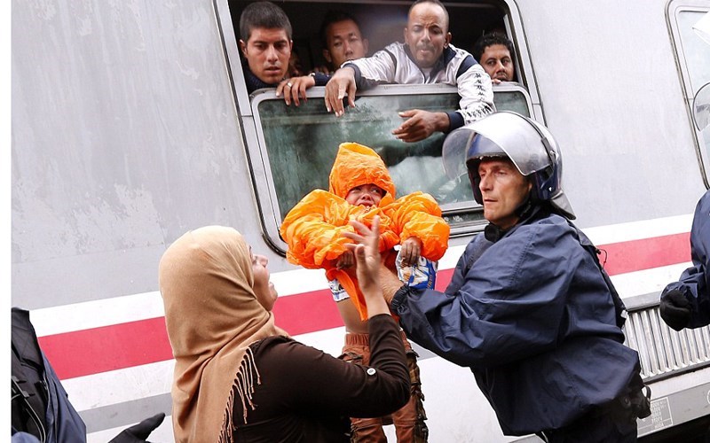 Một cảnh sát giúp đỡ người phụ nữ này bế đứa bé lên một chuyến tàu đến Hungary và Áo. (ảnh: EPA).