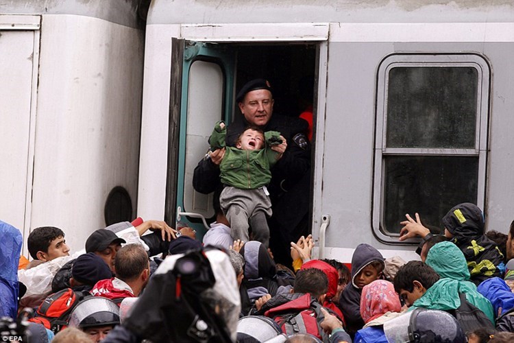 Một em bé được chú cảnh sát đỡ lên tàu giữa đám đông chen chúc, xô đẩy. (ảnh: EPA).
