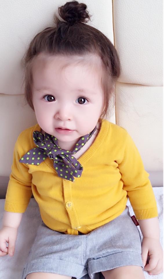 Cô bé được mẹ Elly Trần cho mặc chiếc áo len mỏng màu vàng và buộc khăn quấn cổ.