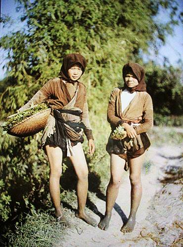 Hai thôn nữ vừa đi hái rau muống, họ mặc áo tứ thân, yếm trắng, đầu chít khăn mỏ quạ.
