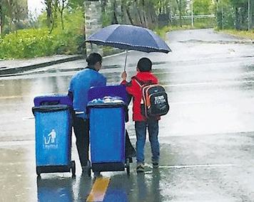 Cậu bé 7 tuổi che ô, kéo xe rác cùng người lao công dưới trời mưa