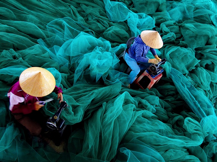 Bức ảnh này khắc họa công việc may vá lưới đánh cá cho chồng của những người phụ nữ miền biển. (Ảnh Lộc Mai)